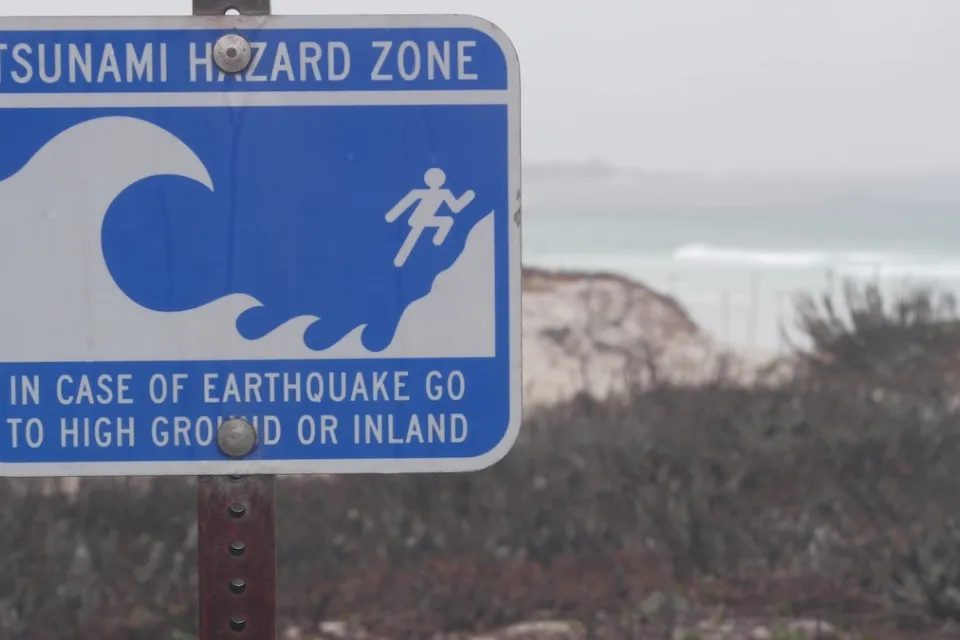 Close-up of blue and white tsunami warning sign on coast in Monterey, California on gloomy day.